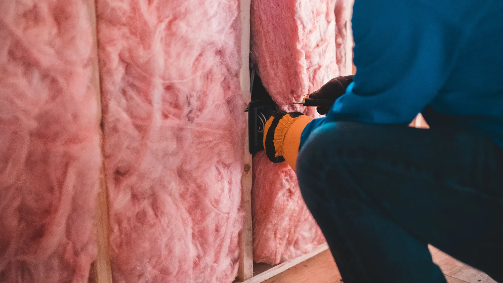Dämmwolle zwischen Holzständern, Hand mit Arbeitshandschuh